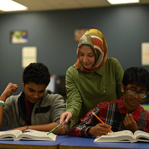 A teacher gives instruction to two high school boys as they work together.